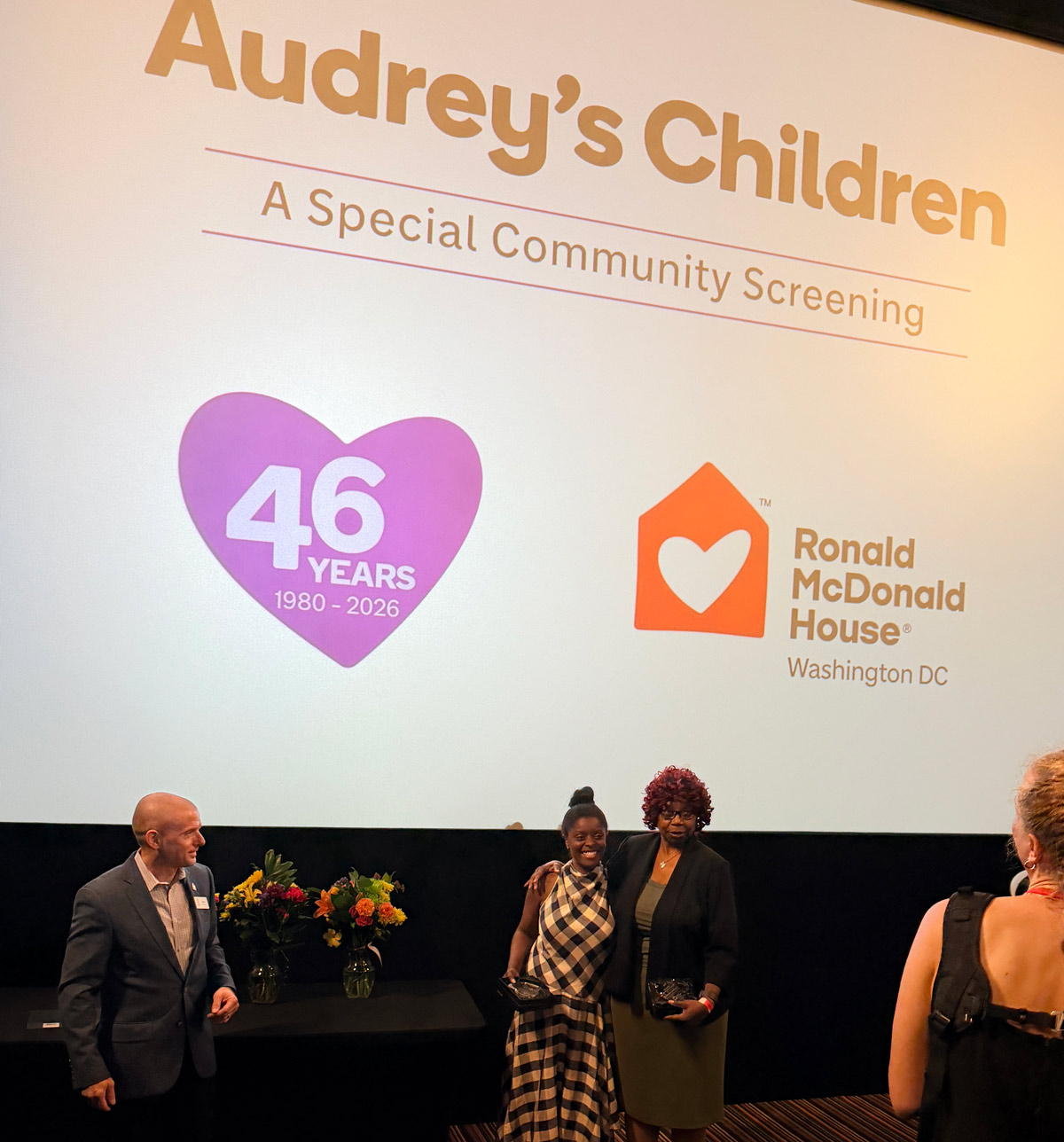 Two volunteer award recipients stand with their recognition plaques after being honored at Ronald McDonald House Washington DC's 46th Anniversary community film screening. Vice President of Community Engagement Josh Bokee stands nearby as guests take photos.